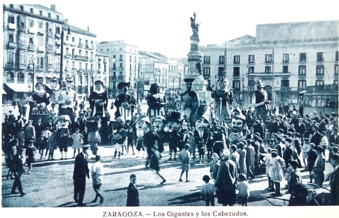 Tarjeta de la decada de los años 30 del siglo pasado, con los Gigantes y cabezudos mezclados con niños y mayores en la plaza central de la ciudad